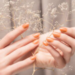 Female hands with glitter beige nail design. Female hands hold dry autumn flower. Woman hands on beige fabric background